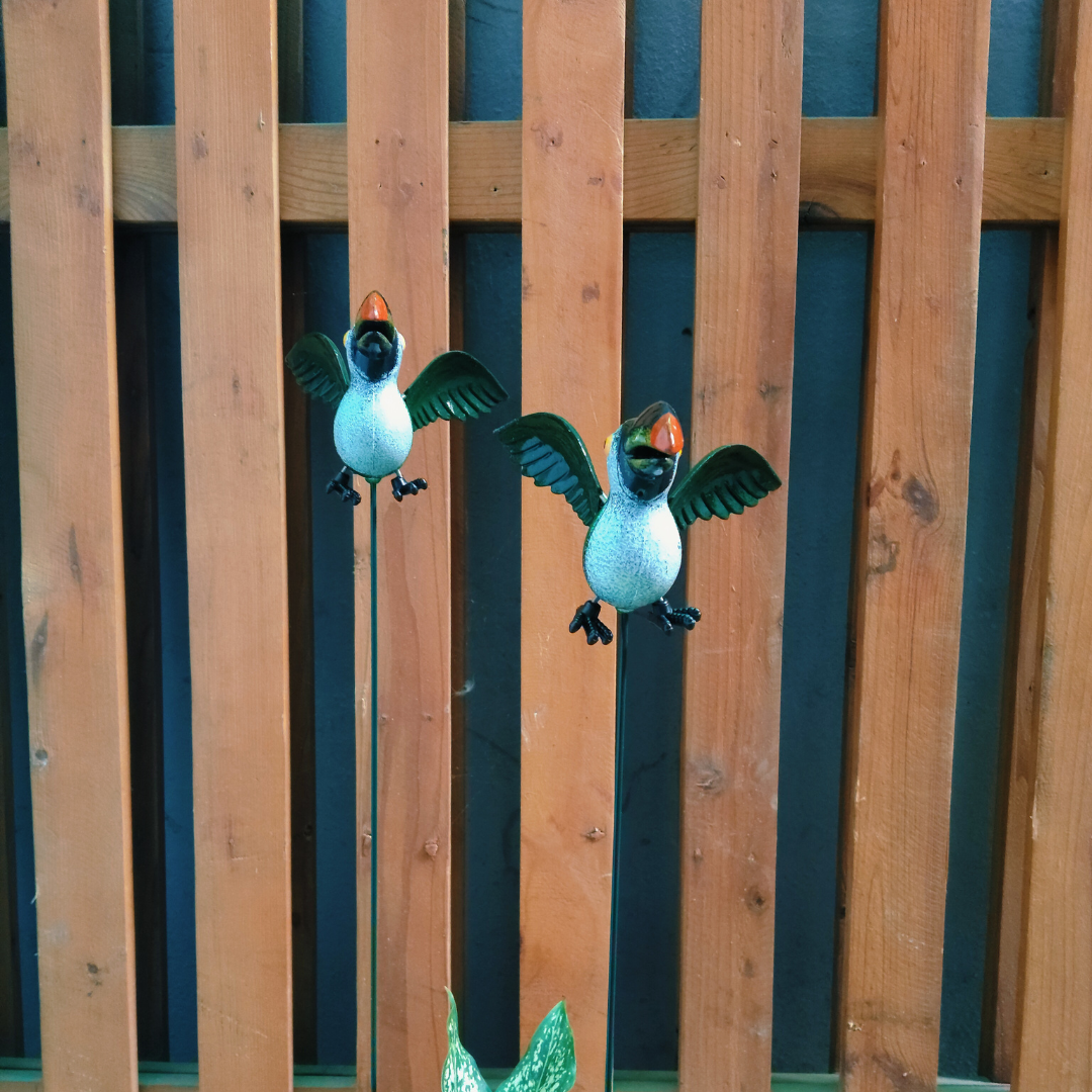 Two decorative penguin figures on sticks against a wooden fence.