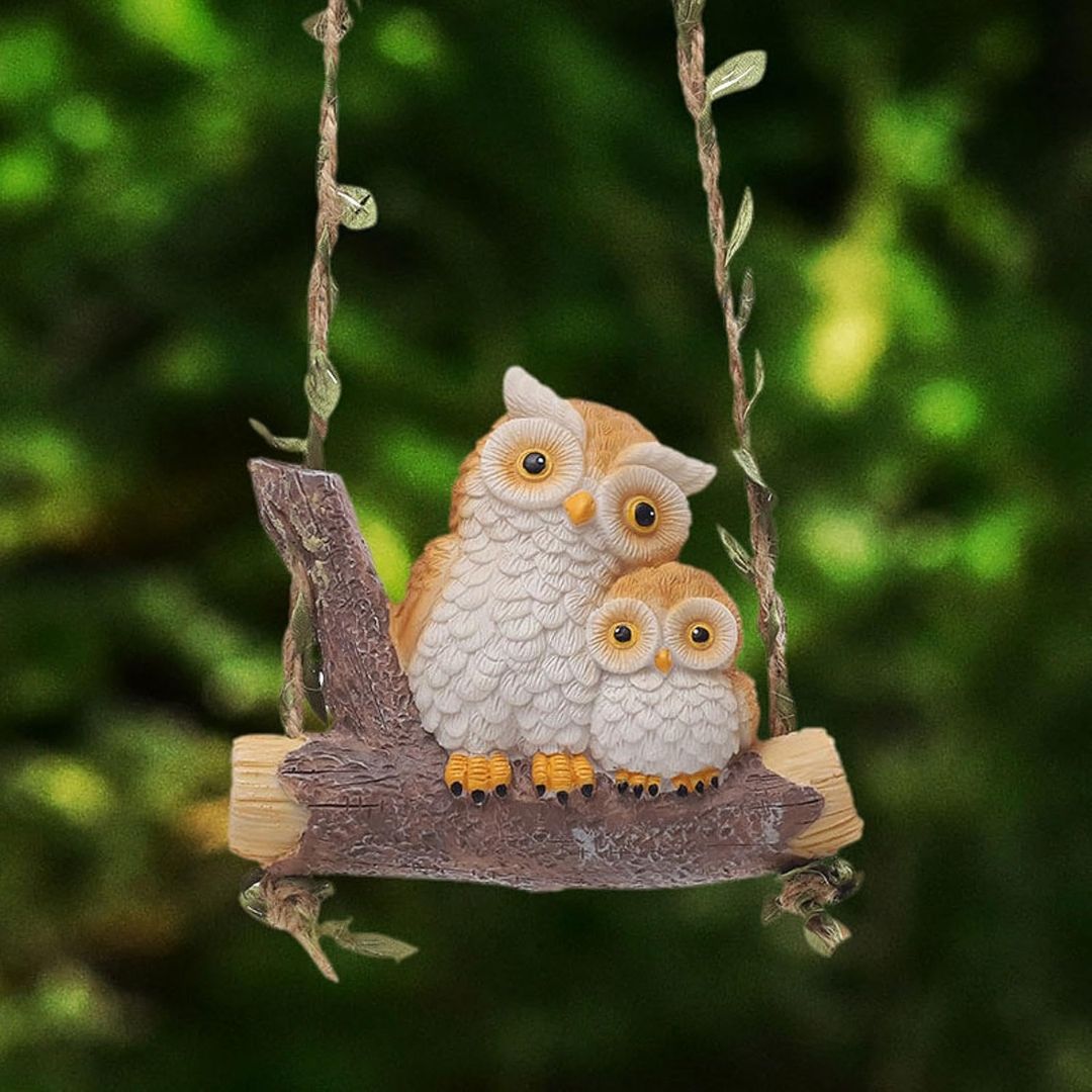 Two owl figurines on a branch against a blurred green background