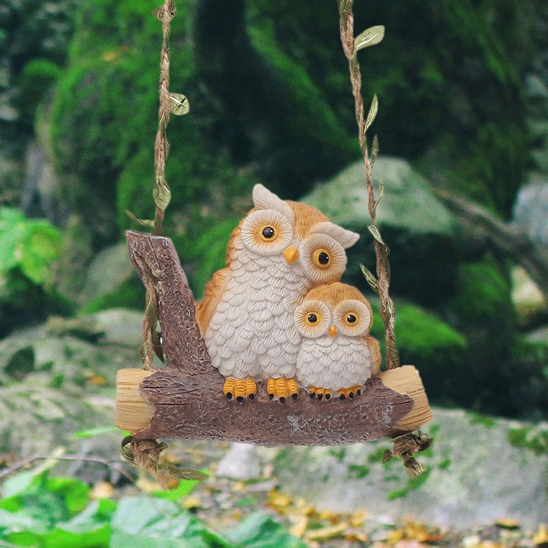 Two owl figurines on a swing with a natural background