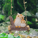 Two owl figurines on a swing with a natural background