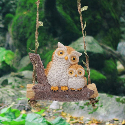 Two owl figurines on a swing with a natural background