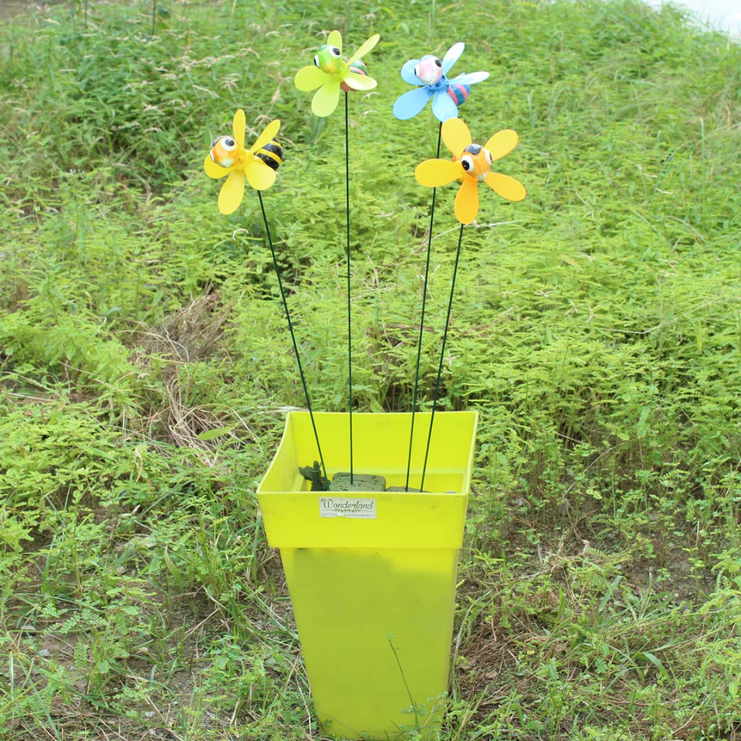 Colorful flower-shaped wind spinners in a green bucket against a grassy background