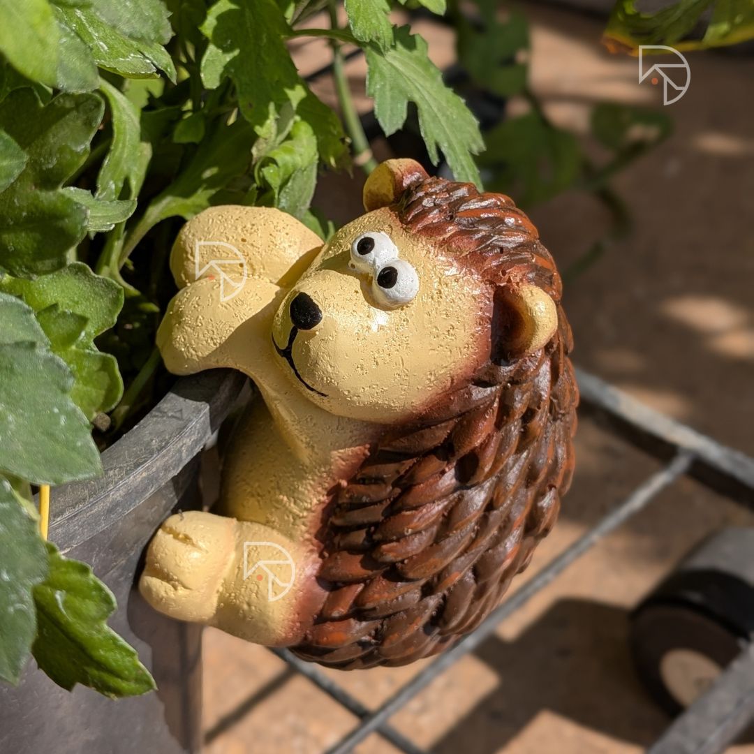Top view of hanging hedgehog garden figurine on pot edge — earthy brown spine detail against green leaves