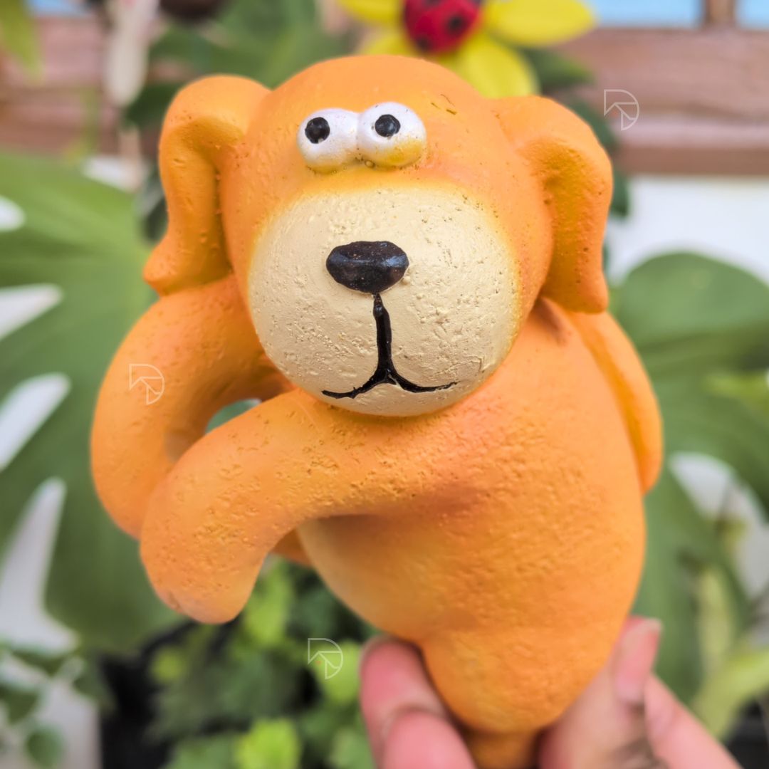 Orange resin dog pot hanger on garden planter with green foliage — balcony pot decoration