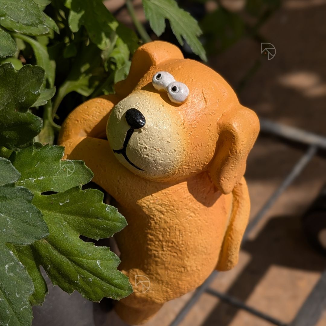 Hanging dog figurine on garden pot rim — side view showing dangling legs and climbing pose
