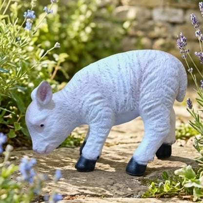 White lamb figurine on a stone surface with plants in the background