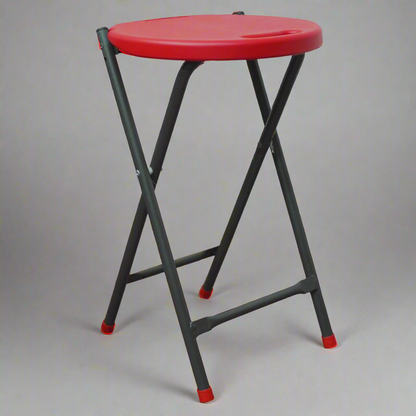 Red stool with black legs on a wooden floor against a textured wall.