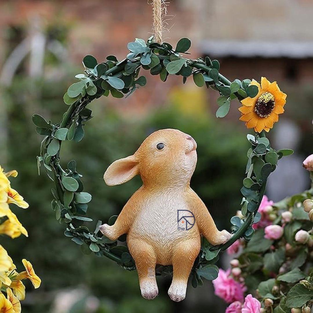 Cute bunny figurine sitting on leafy wreath with sunflower, outdoor garden decor