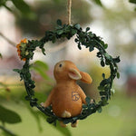 Cute rabbit figurine sitting on a hanging green wreath with artificial leaves and flower