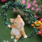 Cute rabbit figurine on leafy wreath swing with artificial sunflower, garden decor