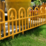 A bright yellow metal garden fence with vertical bars and pointed arch tops, shown outdoors on green grass in front of a large yellow planter.