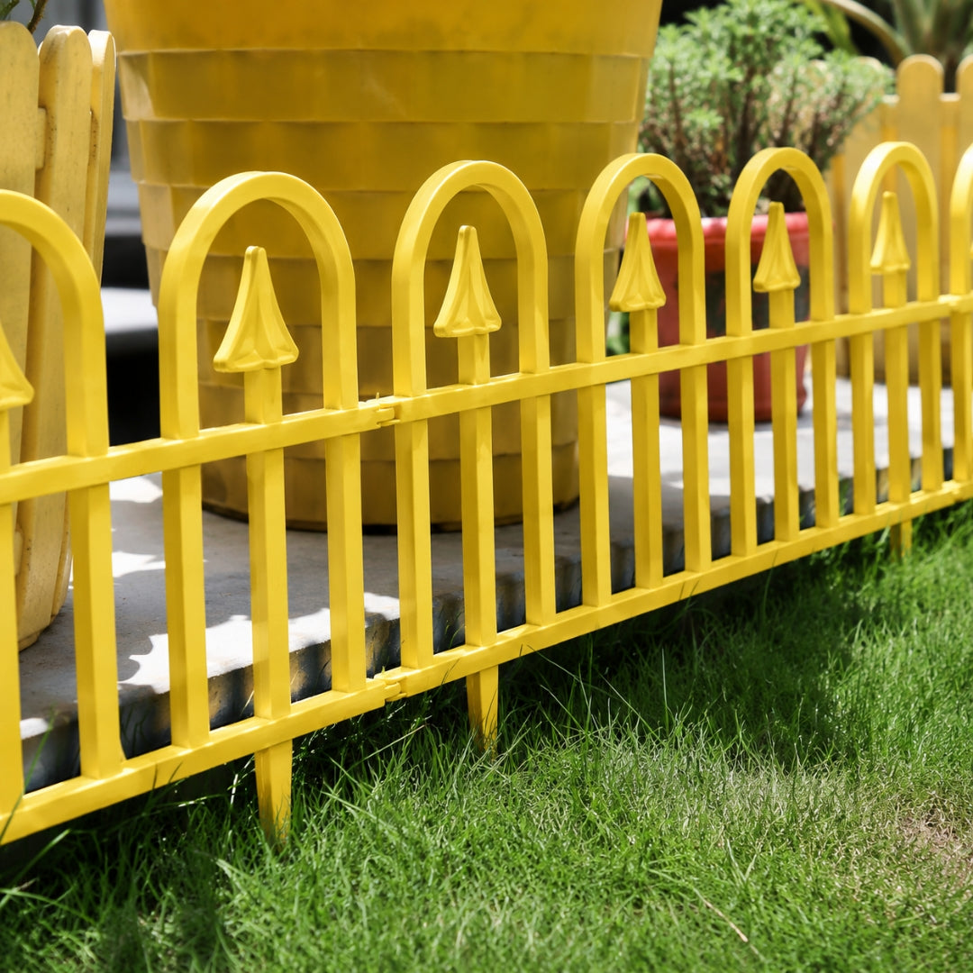 A bright yellow metal decorative fence with pointed tops and arched vertical bars, shown outdoors on green grass in front of a large yellow planter.