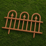 A miniature brown plastic decorative fence with three arched tops and pointed finials, displayed on a green grass background.