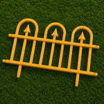 A bright yellow plastic miniature garden fence with three arched pickets and pointed tops, displayed on a green artificial grass background.