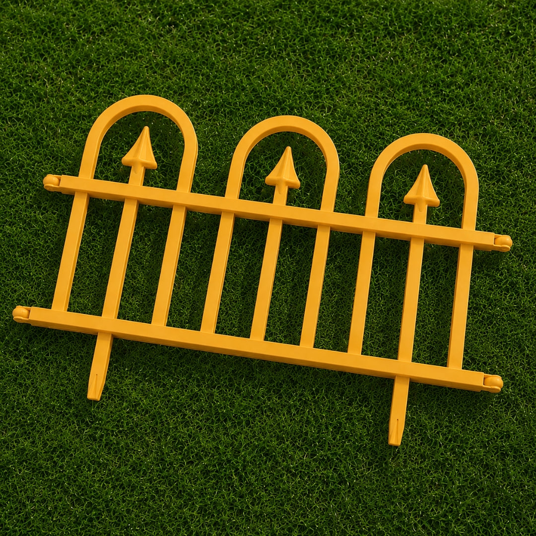 A bright yellow plastic miniature garden fence with three arched pickets and pointed tops, displayed on a green artificial grass background.