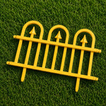 A bright yellow miniature decorative fence panel with three arched tops and pointed finials, displayed on a green grass-like surface.