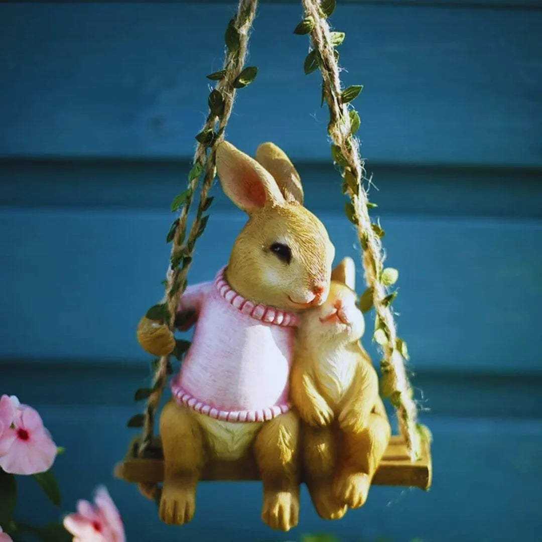 Cute rabbit figurines on a swing with pink flowers and blue background, garden decor