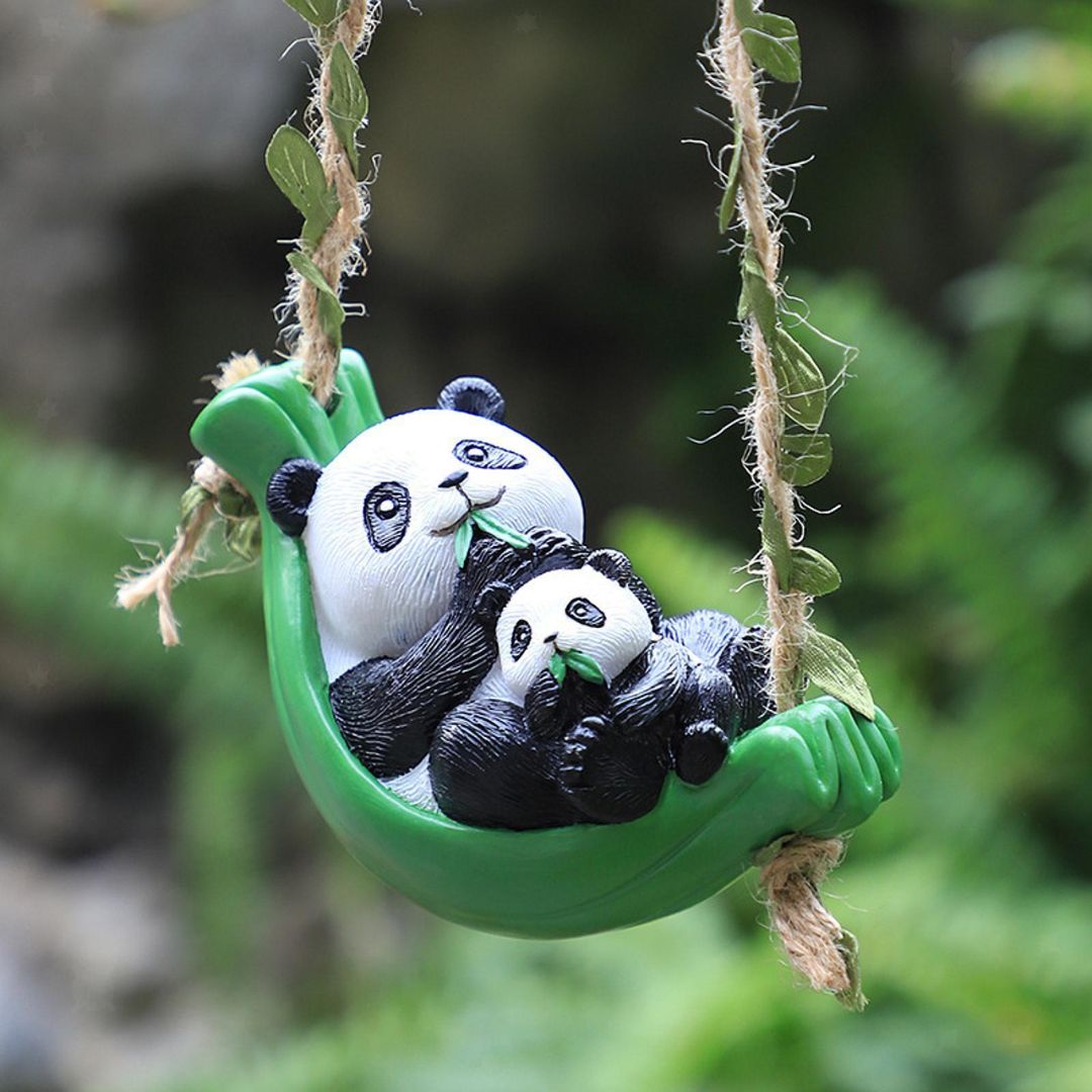 Two panda figurines on a green swing with a blurred natural background
