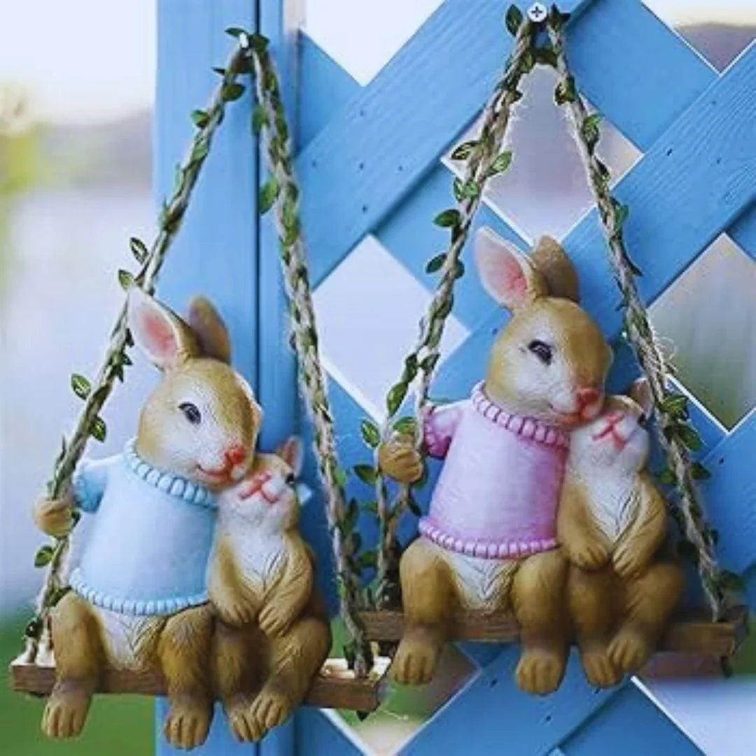 Cute bunny figurines in sweaters sitting on swings, outdoor garden decor against blue lattice.