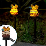Solar garden pathway light with yellow bird figurines and 'welcome' sign, glowing at night