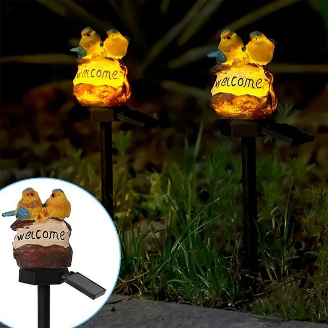 Solar garden pathway light with yellow bird figurines and 'welcome' sign, glowing at night