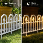 A split comparison showing a white decorative picket fence in daylight on the left and the same fence lit at night on the right. The right side includes a moon icon with the text 'Night (LED Lights On)' and shows warm yellow lights glowing through the fence posts onto grass and a large potted plant in the background.