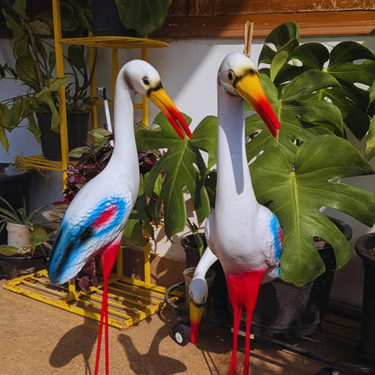 Two decorative storks with colorful plumage standing among plants.
