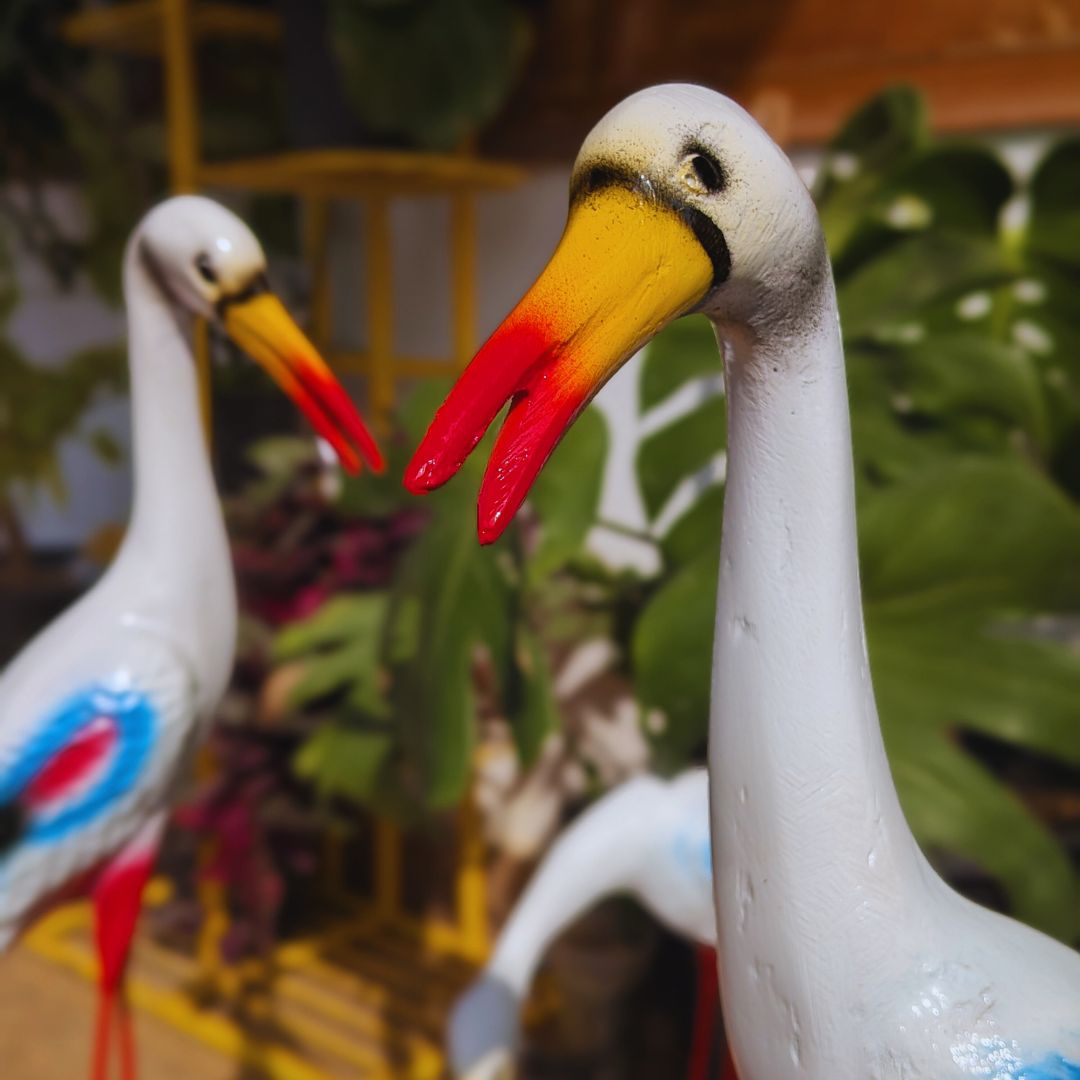 Two ceramic storks with colorful beaks against a blurred green leafy background