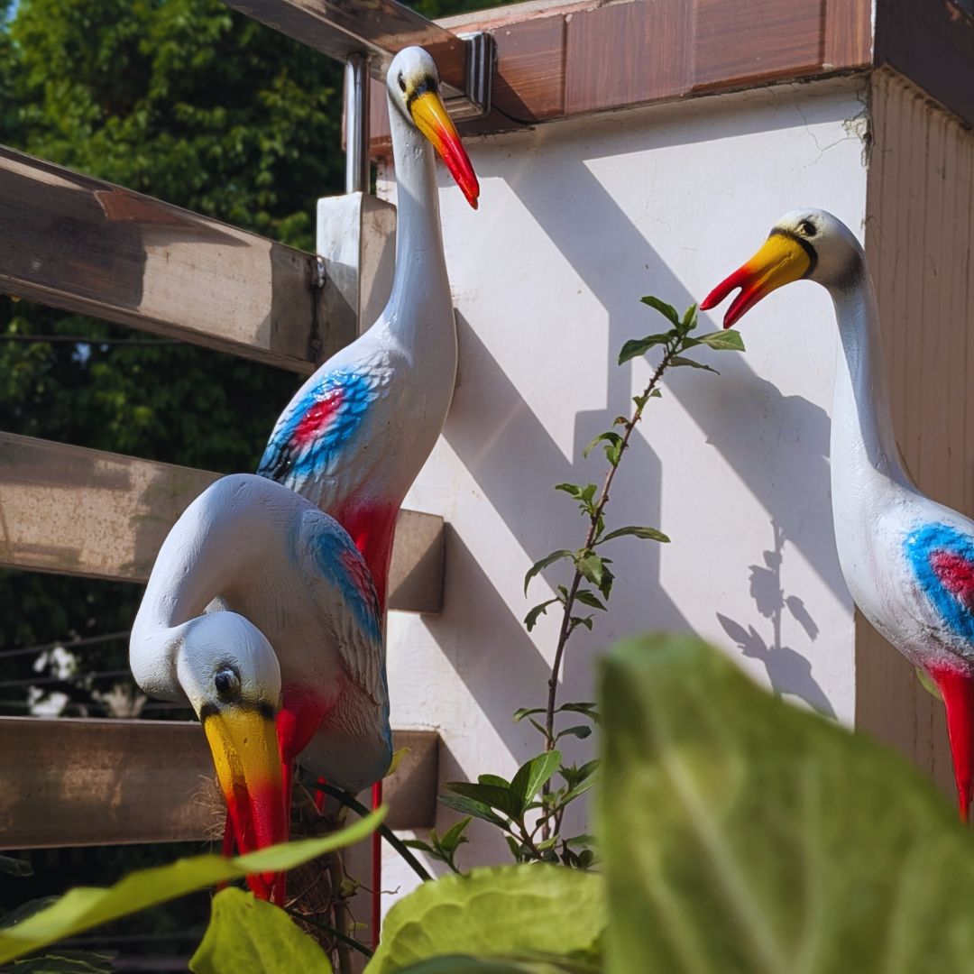 Decorative bird statues on a wall with greenery in the foreground