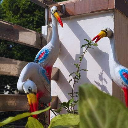 Decorative bird statues on a wall with greenery in the foreground