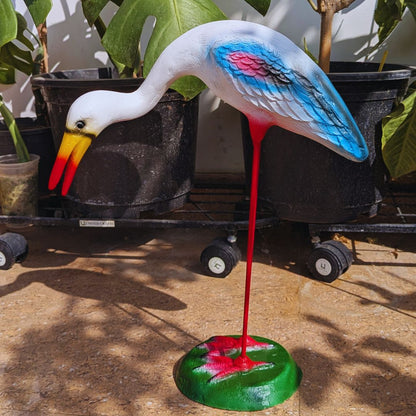 Colorful bird sculpture on a stand with plants in the background
