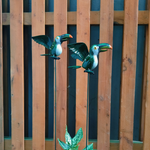Two decorative toucan figures on sticks against a wooden fence.