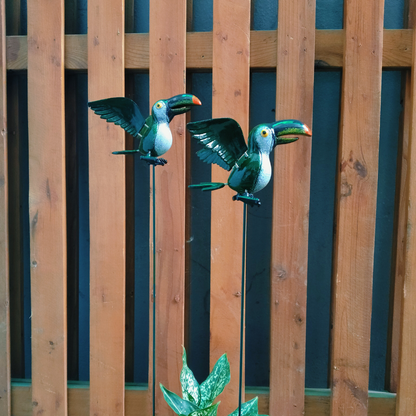 Two decorative toucan figures on sticks against a wooden fence.