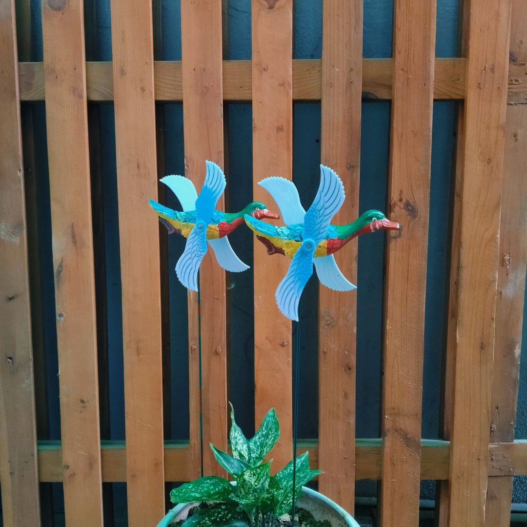 Colorful bird-shaped wind spinners against a wooden fence.