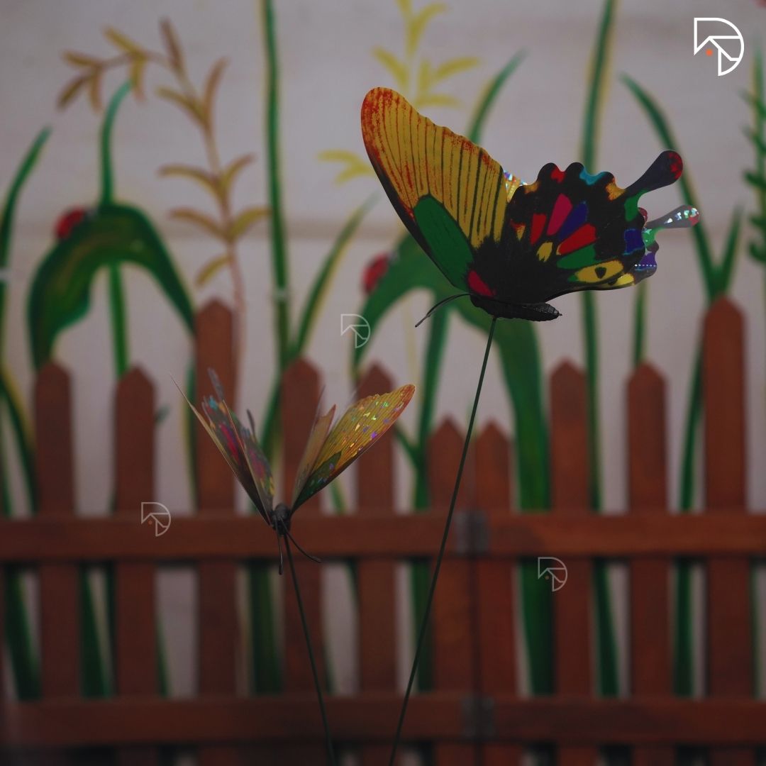 Colorful butterfly-shaped garden stake against a wooden fence and grass background