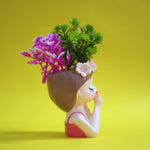 Decorative vase shaped like a person with flowers on a yellow background