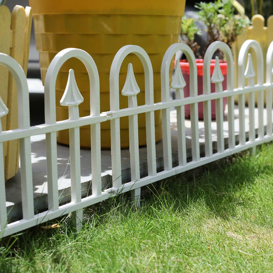 A white decorative fence made of PVC installed on grass, featuring pointed arch designs.