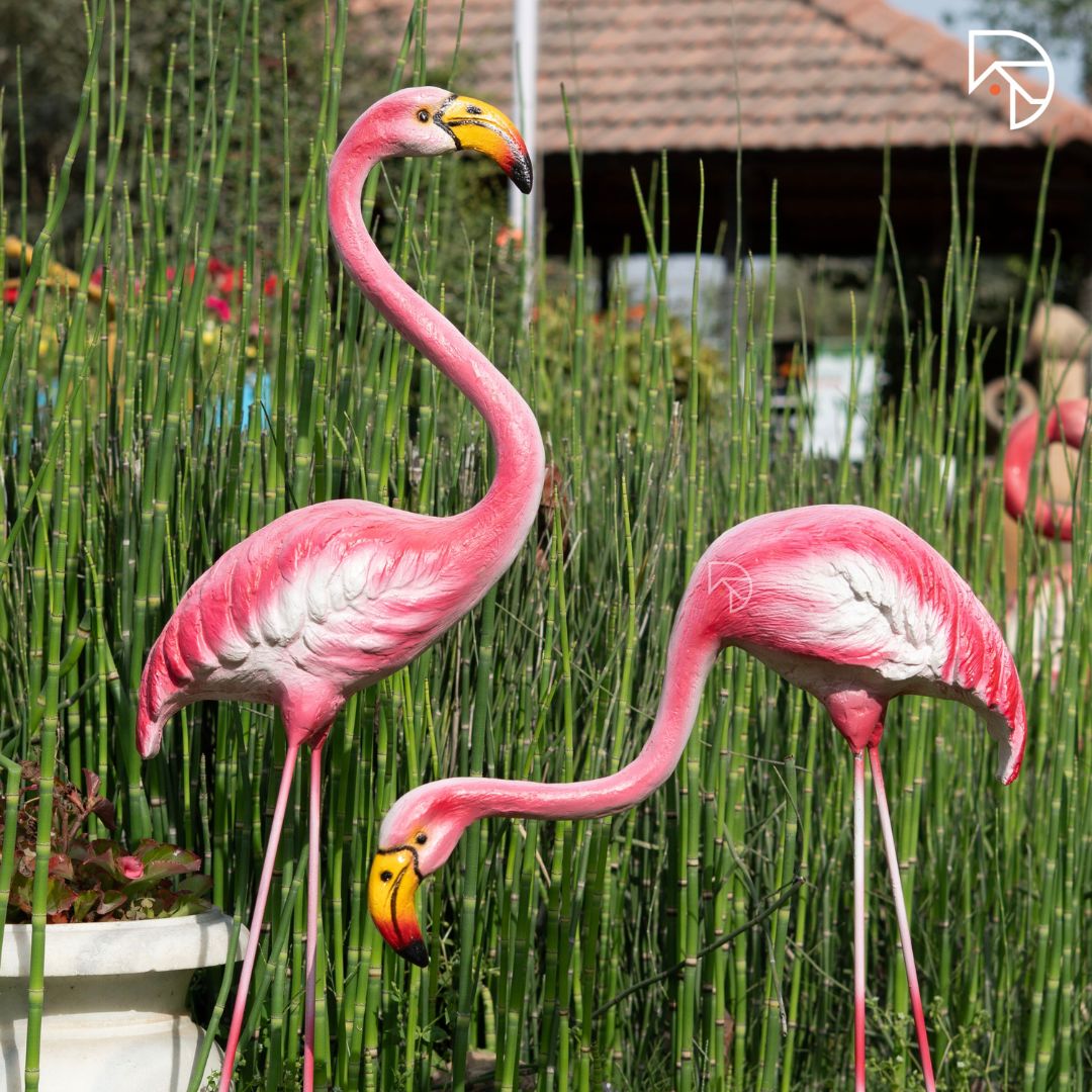 Two pink flamingo statues in a garden setting with greenery.