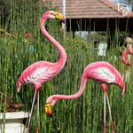 Two pink flamingo statues in a garden setting with greenery.