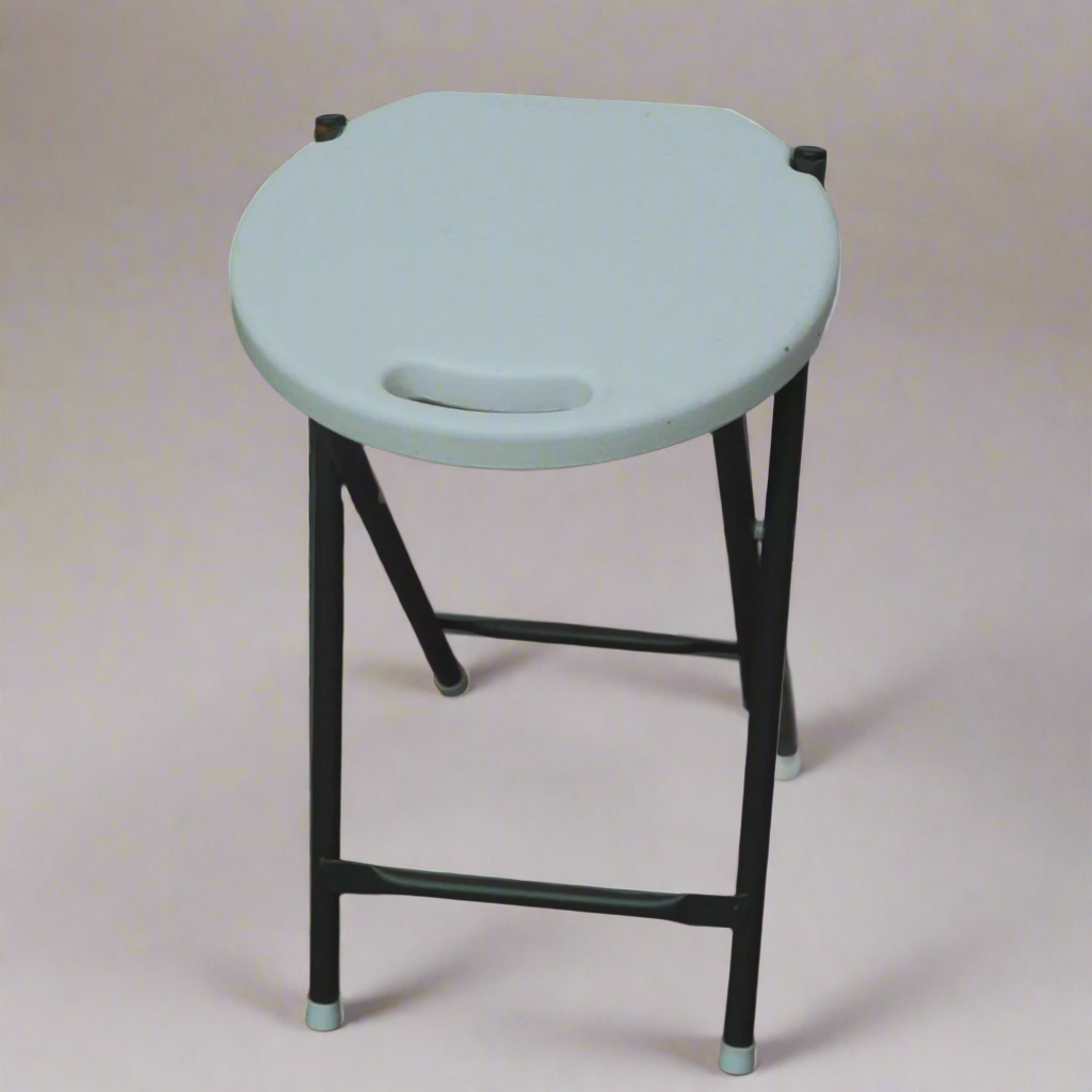 White stool with black legs on a wooden floor against a stone wall.