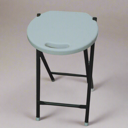 White stool with black legs on a wooden floor against a stone wall.