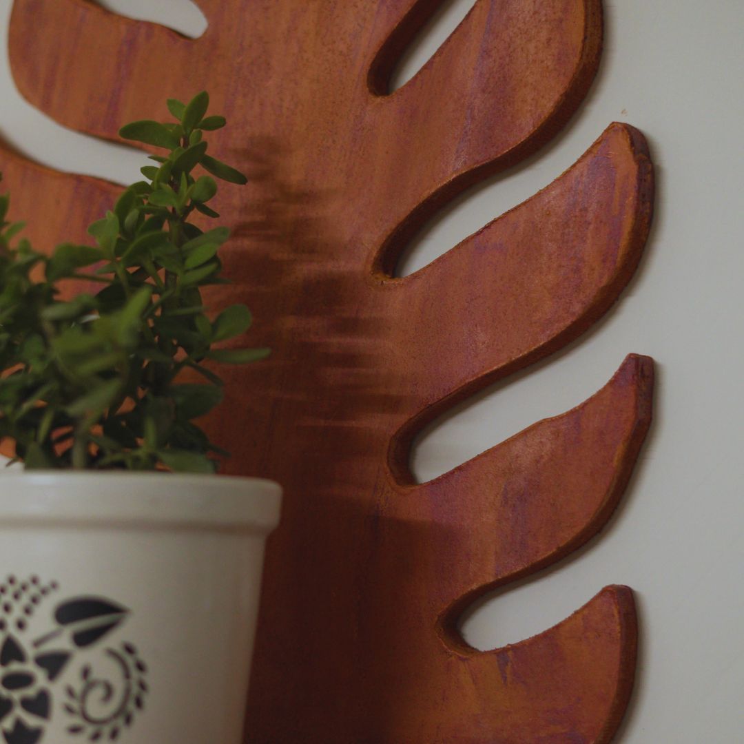 Decorative wall art with a large leaf design and a potted plant in the foreground.