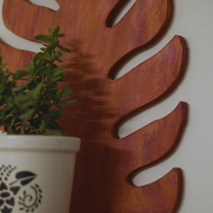 Decorative wall art with a large leaf design and a potted plant in the foreground.