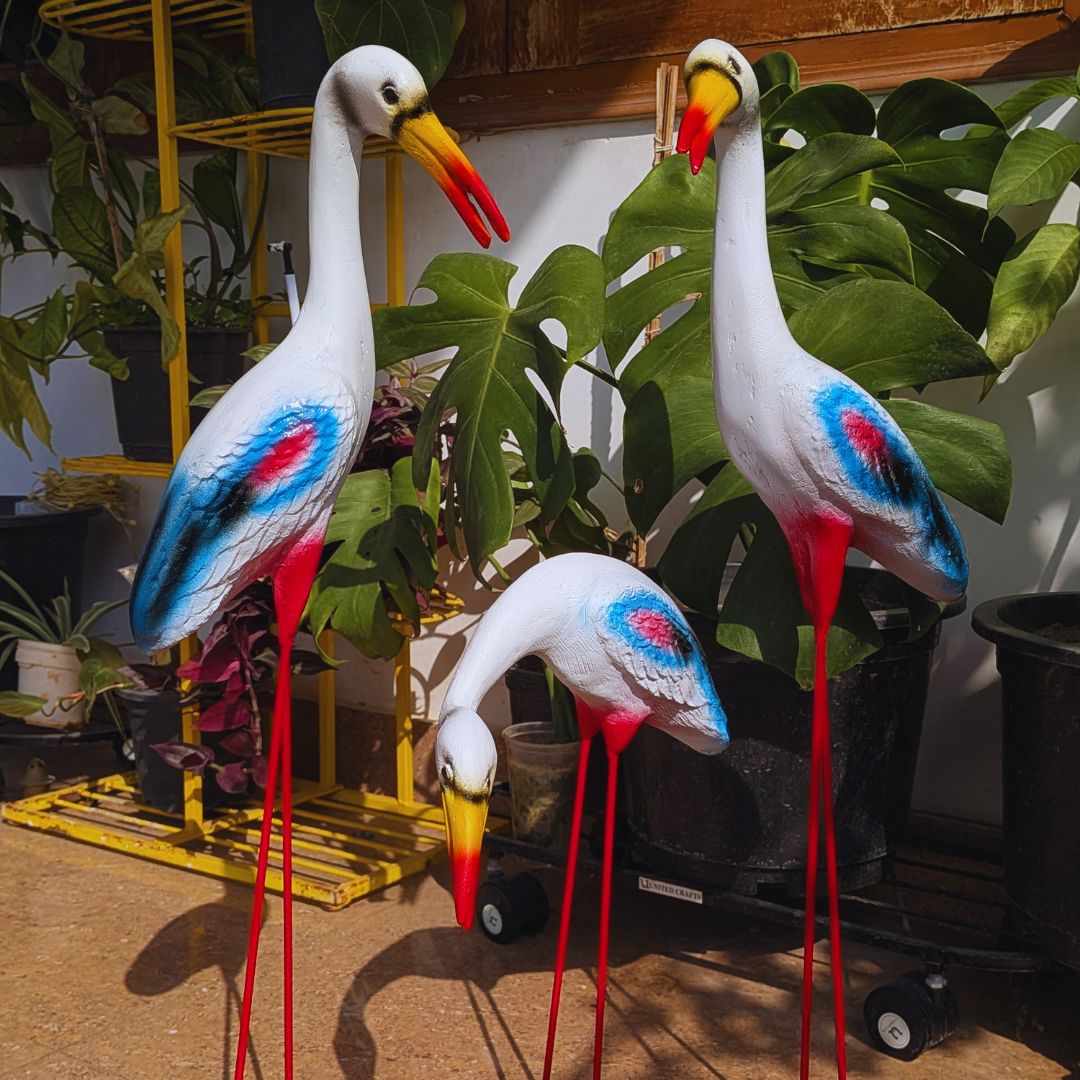 Decorative flamingo statues with red, blue, and yellow colors in a garden setting.